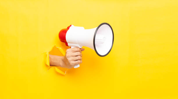 istock man hand holding a megaphone on yellow  background 2194727024