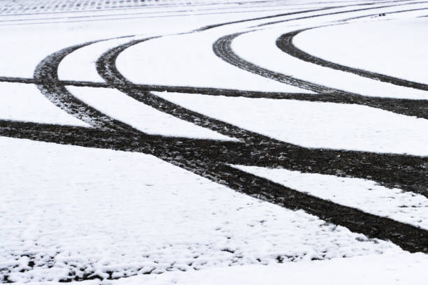 Close-up of vehicle tire tracks creating intersecting patterns on snow-covered ground during winter season, showcasing texture and wintertime themes.