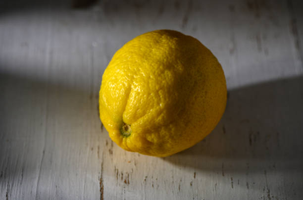 istock Bright yellow lemon resting on a rustic wooden surface in soft sunlight 2194728223