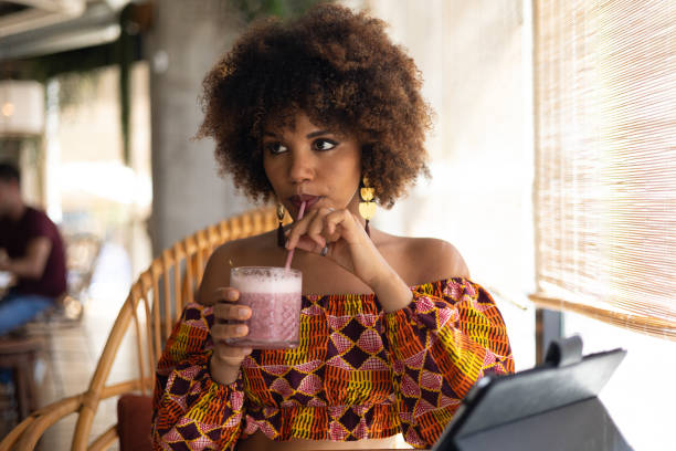 istock Stylish young african woman drinking a smoothie and using a tablet in a trendy cafe 2194735962