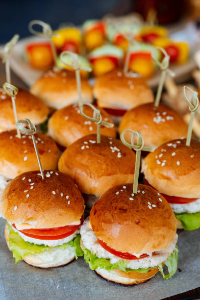 istock A delightful assortment of mini hamburgers, elegantly displayed on toothpicks, is arranged beautifully on a table, showcasing a variety of flavors and ingredients for everyone to enjoy 2194739031