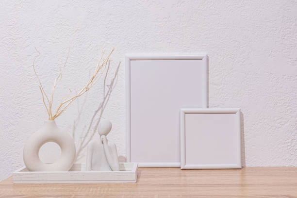 istock Stylish home interior in white tones. Two empty white photo frames, a vase with dry branches, a figurine of thought made of concrete. Wooden surface. 2194739240