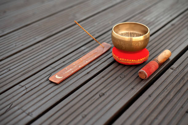 Tibetan singing bowl with a mallet and incense holder on a wooden surface.
