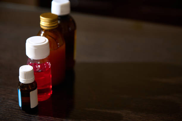 Assorted medicine containers containing different colored liquids arranged on a wooden table.