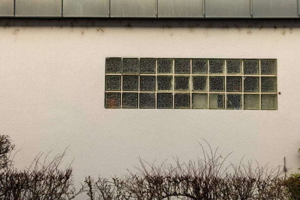 Glass block window adorned with fading graffiti on a plain wall in an urban setting during daylight