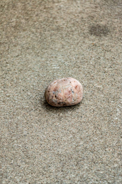 Close-up view of a single round and smooth stone resting on a rough grey concrete background. The simplicity showcases the natural materials and textures, evoking thoughts of nature and minimalism.