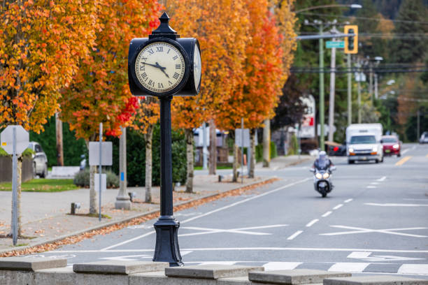 A quaint street at Harrison Lake, BC, featuring a vintage clock and vibrant autumn leaves. A motorcycle rider adds dynamic movement to the scene under a clear sky.