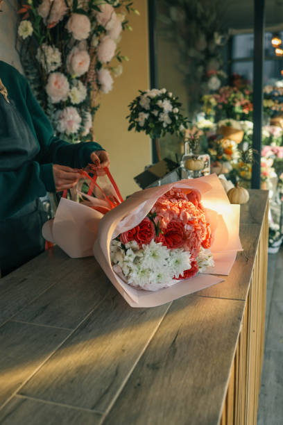 istock Close-up of a luxurious bouquet featuring vibrant red roses, delicate hydrangeas, and white alstroemerias, elegantly arranged and wrapped in soft pastel paper on a wooden counter 2194752386