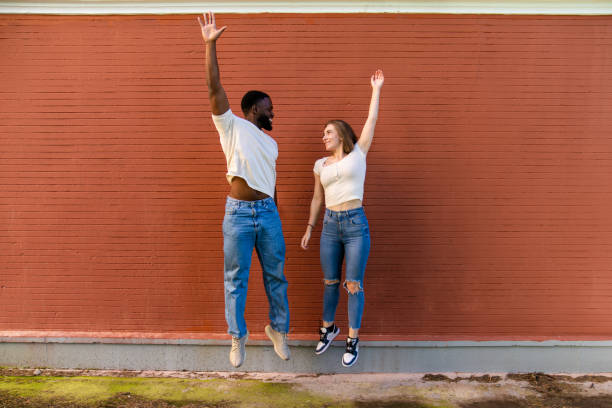 istock Multiethnic couple jumping with raised arms in front of brick wall 2194757665