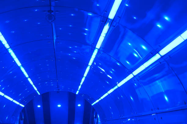 Interior of a tunnel or passageway with a curved ceiling made of reflective, metallic panels. Ceiling is lined with fluorescent lights that create a modern and futuristic appearance