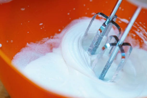 istock metal mixer whisks beating a translucent egg white into a stiff white foam, set against a vibrant orange bowl, showcasing the process of baking and food preparation 2194765642