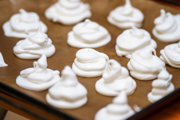 Delicate meringue peaks rest on a baking tray, ready for baking. These fluffy white confections made from whipped egg whites and sugar are perfect for desserts