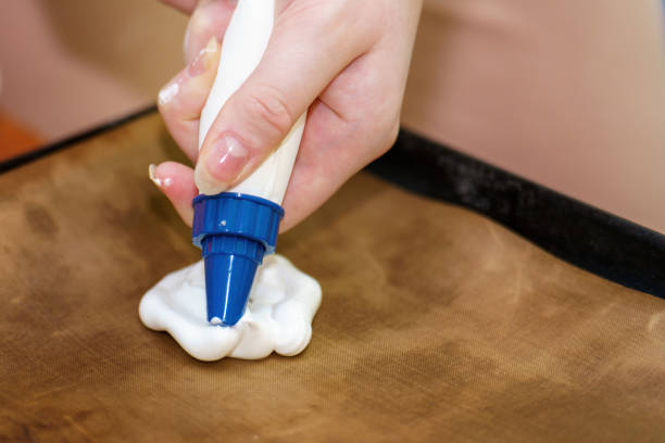 istock hand squeezing a piping bag with a star tip, releasing a white meringue mixture made from whipped egg whites and sugar onto a baking tray, ready for baking 2194765644
