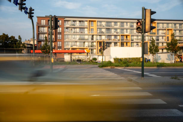 Blurred motion of a yellow vehicle crossing a city intersection under a red traffic light. Modern apartment buildings are visible in the background, creating a vibrant urban scene.