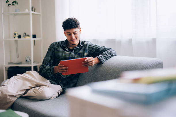 Young Man Reading a Tablet While Relaxing on a Sofa at Home