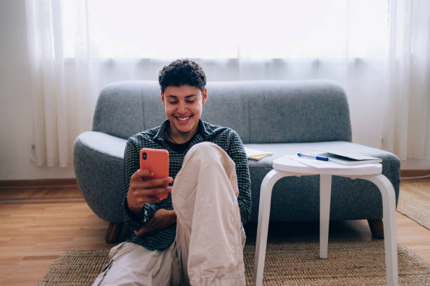 istock Young Man Smiling While Using a Smartphone in a Cozy Living Room 2194772899
