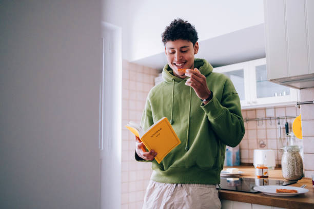 Young Man Reading a Book While Enjoying Breakfast in the Kitchen