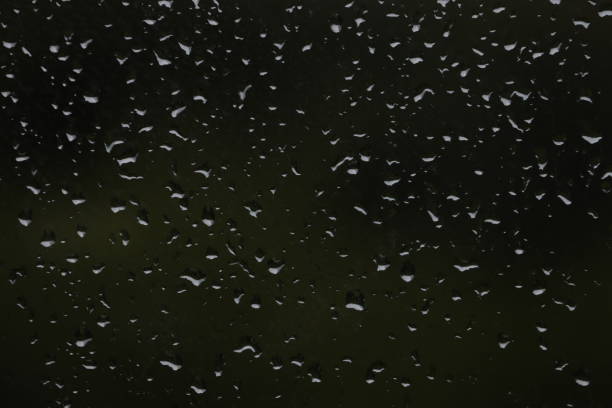 Small drops of water on dark glass close-up.