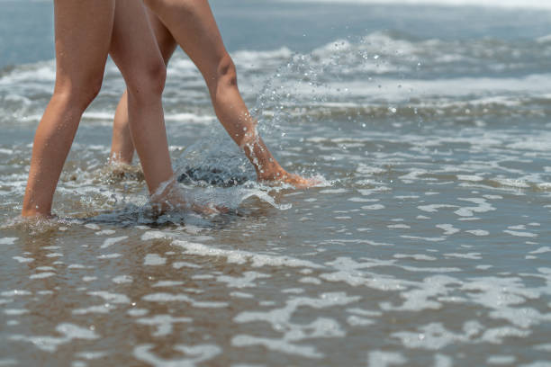 Two young women are walking on the beach, enjoying the refreshing ocean waves on their legs during a summer vacation