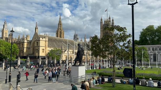 London, United Kingdom - May 29, 2024: People seen walking and sitting at the Parliament Square Garden, with the Westminster Hall in the background and the statue of Sir Winston Churchill.