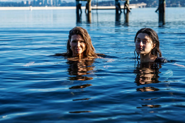 Two Women Partake in an Invigorating Healthy Cold Plunge in a lake.  This activity provides improved circulation, reduced inflammation, and enhanced mental clarity.  This was a cold day 32 degrees Fahrenheit with a water temperature of 54.  Images captured at Mt Baker Park Beach on Lake Washington Seattle.