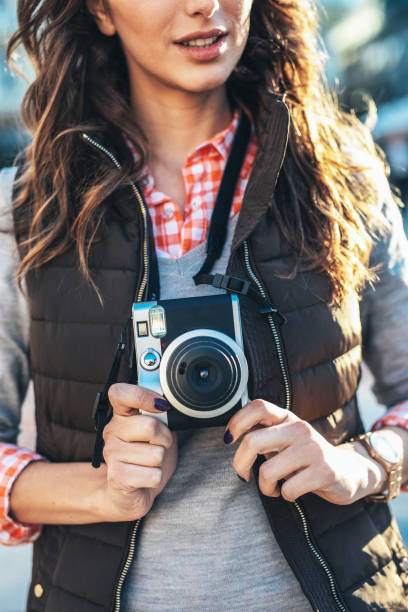 Close up of girl photographer  with camera in her hands taking photos in the city. She is wearing casual clothing, taking photos with her beautiful analog film camera. Close-up image of urban female photographer