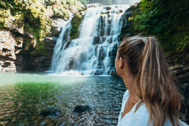 Woman sitting by cascading waterfall, enjoying tranquil view. Relaxation and nature exploration.