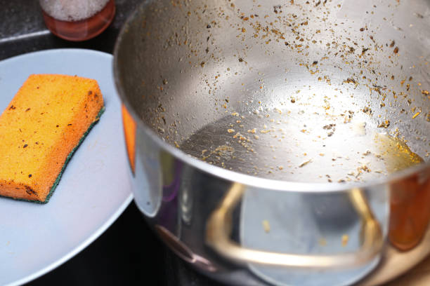 Dirty greasy metal pot with sponge for dishwashing. Cleaning tasks kitchen interior. Stubborn stains removal.