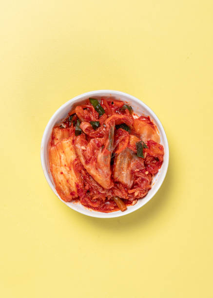 istock A small white bowl filled with traditional Korean kimchi, placed on a vibrant yellow background. The fermented napa cabbage is covered in a red spicy seasoning, highlighting its rich texture and flavor 2194806892