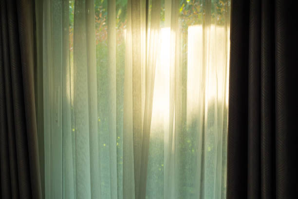 Soft light on curtains window. There was morning light through the window in room, looking at the view of the mountains and trees as the sun rose.