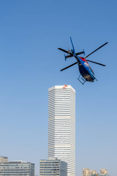 A helicopter can be seen above a skyscraper with a blue sky as a background. It gives an urban image.