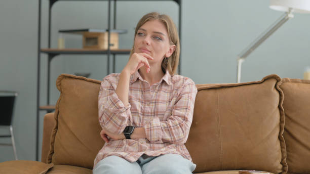 istock Pensive Young Woman Sitting on Sofa at home 2194814001