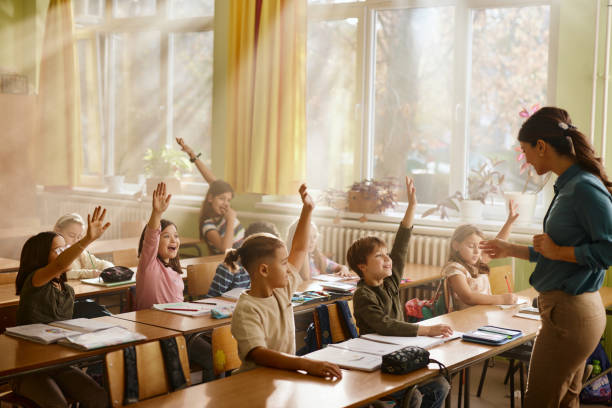istock Happy school kids raising hands on a class in the classroom. 2194815360
