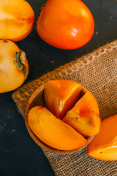 istock Rustic composition with fresh persimmons in a wooden bowl and on a dark textured background, accented by burlap. Ideal for seasonal, culinary, and rustic lifestyle themes 2194816552