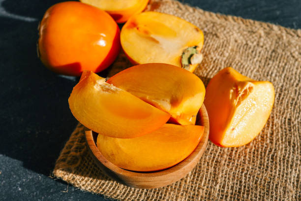 istock Sliced and whole persimmons arranged on a dark textured surface with natural light and burlap, showcasing vibrant colors and rustic simplicity. Perfect for food, seasonal, and healthy living themes 2194816561