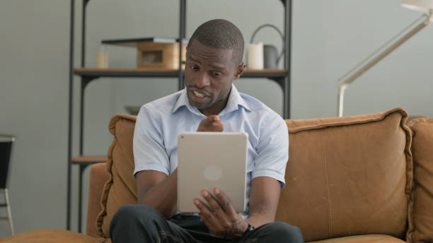 istock African Man Doing Video Chat on Tablet while Sitting on Sofa at Home 2194822237