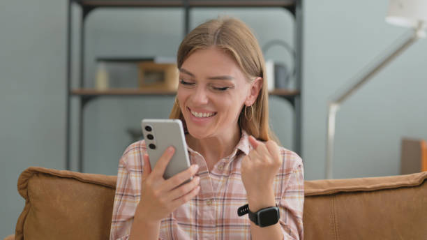 istock Young Woman Enjoying Success on Phone while Sitting on Sofa at Home 2194825185