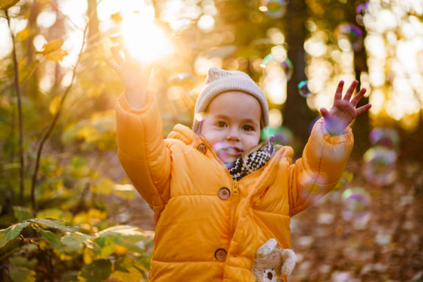 Cute little girl is playing with bubbles during an autumn day in the forest