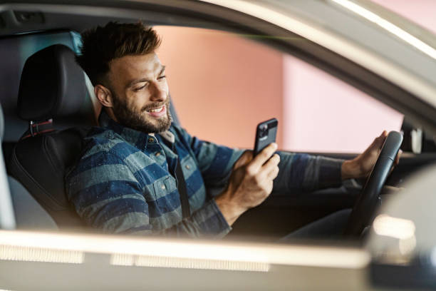 istock Smiling handsome driver typing message on his cellphone and smiling at it while driving a car. 2194827270