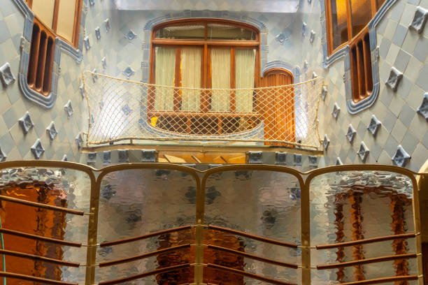 Light filtering through textured glass panels illuminates the unique blue tiled walls and wooden balcony of casa batllo, showcasing antoni gaudi's architectural brilliance
