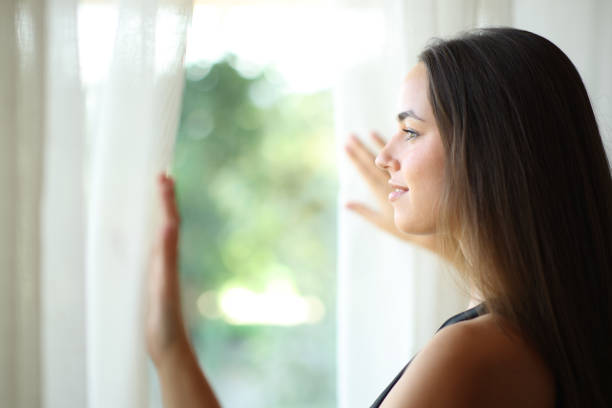 istock Woman looking through a window in a house 2194829476