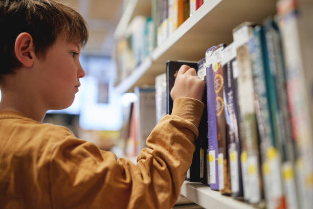 Close-up of a boy selecting a book from a library shelf.