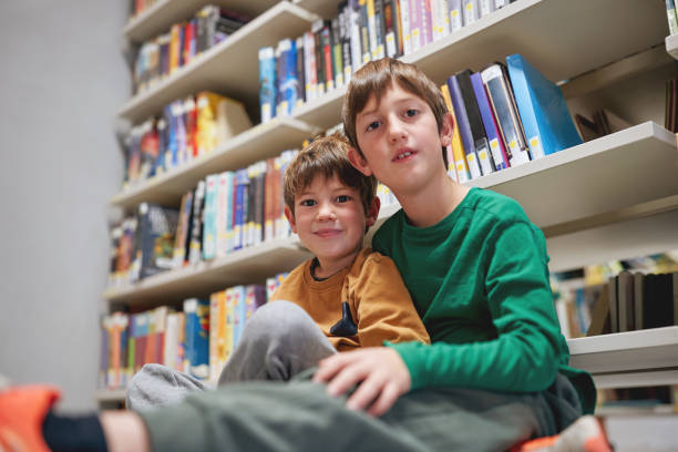 Two smiling boys sitting together in a library.
