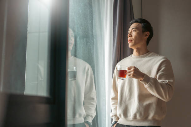 Young Asian Chinese man having cup of coffee while standing at home. stock photo