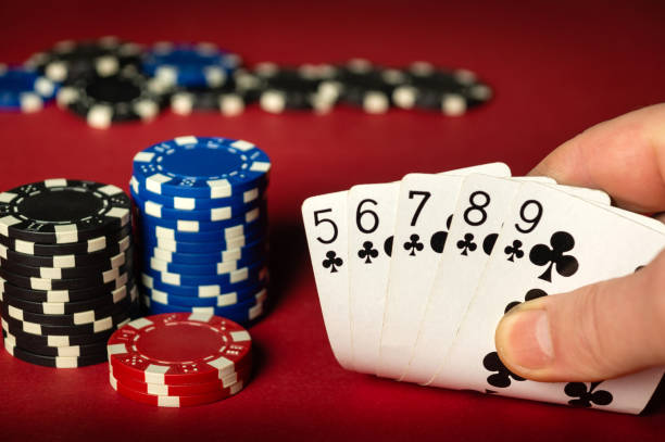 istock Player holds playing cards with winning straight flush combination on red poker table. Close-up of playing chips and hand with cards on table in club. 2194831756