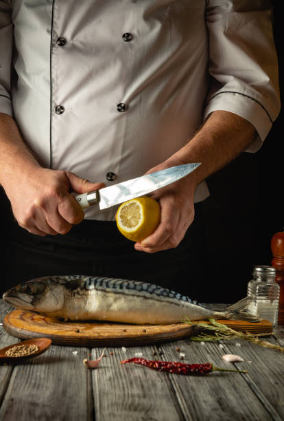 istock A skilled chef skillfully slices a lemon while preparing fresh fish on a wooden cutting board. Surrounding ingredients include spices and herbs, enhancing the culinary experience 2194831944