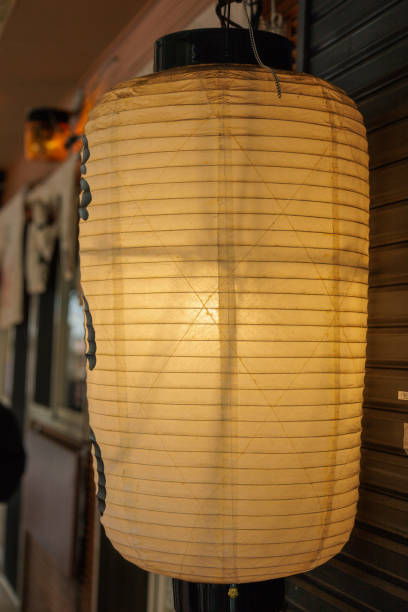 A traditional Japanese chochin paper lantern is softly illuminated, showcasing its delicate ribbed structure. The warm glow creates a cozy and inviting atmosphere for New Years arcade visitors.