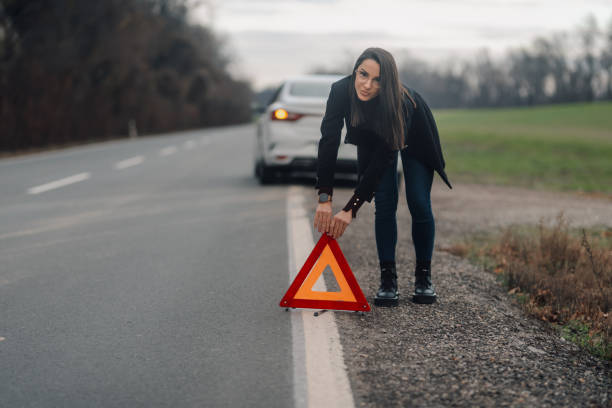 istock Businesswoman placing warning triangle after car breakdown on road 2194832510
