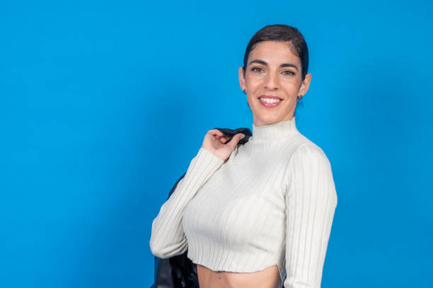 Smiling woman holding leather jacket on blue background