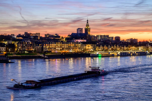 Skyline of the city Nijmegen on the riverbank of the Waal seen from the Waalbrug during sunset. Various ships are passing the river during this beautiful cold winter sunset during the blue hour at the end of the day.